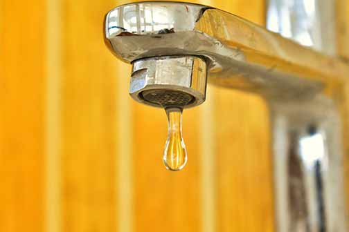 Close-up photo of a water drop falling from a leaky faucet.