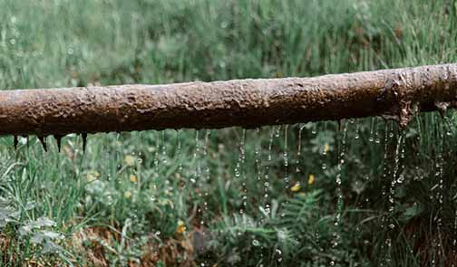  Rusted, leaking pipe above a grassy meadow.