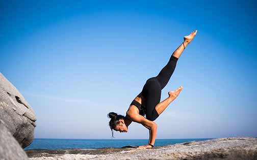 A woman doing yoga on a rock near a body of water.