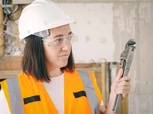 A female wearing an orange safety vest while holding a wrench