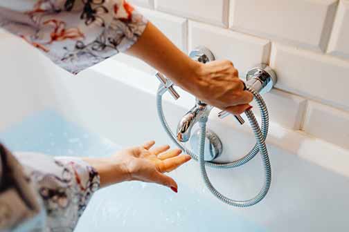  A person opening a faucet of a bathtub