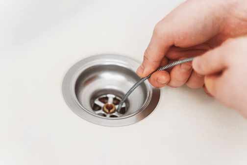 a man using a drain snake to unclog his bathroom sink