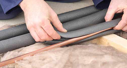 a man installing insulation on his older home pipes