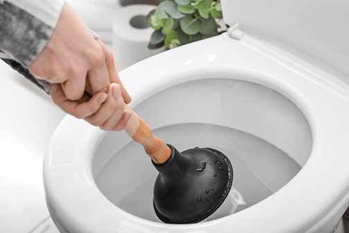 a man fixing a toilet clog with a plunger.